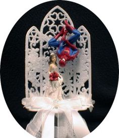 a wedding cake topper with spiderman and bride on it's back, in front of a gothic - styled arch