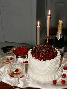 a white cake with cherries on it and two wine glasses sitting next to it