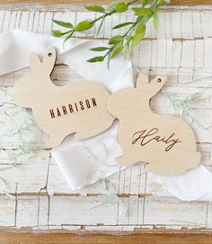 two wooden rabbits with names on them sitting next to some napkins and green leaves