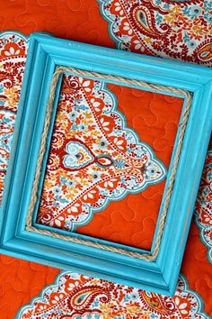 two blue frames sitting on top of an orange and red fabric covered table with paisley designs