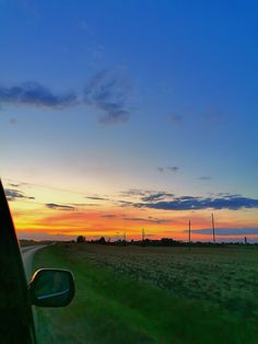 the sun is setting over an open field with grass and power lines in the distance