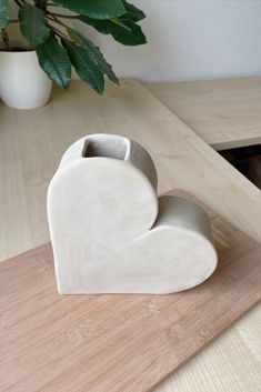 a white heart shaped vase sitting on top of a wooden table next to a potted plant