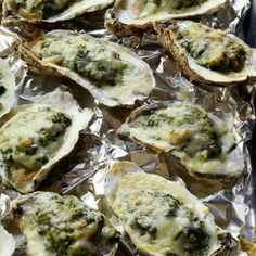 several oysters covered in cheese and broccoli on aluminum foil with sauce sprinkled on them