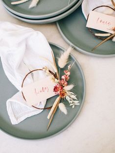 three plates with napkins and place cards on them sitting on a white table cloth