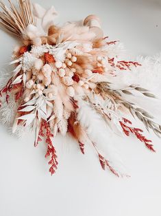 an arrangement of dried flowers and feathers on a white surface