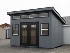 a small gray building sitting on top of a parking lot next to two other buildings