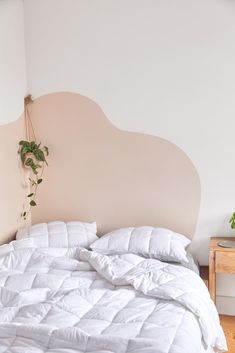 an unmade bed with white comforter and pillows on the headboard next to a plant