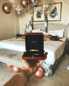 a person holding up a ring in front of a bed with balloons hanging from the ceiling