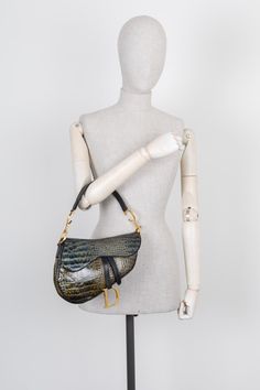 About: 1999 entwarf John Galliano entwarf die unverkennbare Saddle Bag. Die Tasche wurde nach ihrem ersten Debüt für die SS 2000 Kollektion in kürzester Zeit zur It-Girl Accessoire. Ihr grosses Comeback feierte die Ikone als sie in Kim Jones' erster Kollektion für Dior Homme, und auch in Maria Grazia Chiuris FW 2018 Kollektion zu sehen war. Jahr: 2001 Made In: Italy Masse: B 25 x H 19 x T 6 cm Handle: 50 cm Material: Leder mit Krokodil Prägung Farbe: Smaragd Hardware: Gold Innen- & Aussenfächer: Designer Saddle Bag With Removable Pouch, Designer Saddle Shoulder Bag With Palladium Hardware, Designer Evening Saddle Bag, Luxury Saddle Bag With Palladium Hardware, Maria Grazia, John Galliano, Burberry Bag, Fendi Bags, Saddle Bags