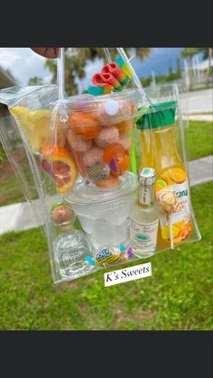 a person holding a clear plastic bag filled with fruit and drinks on the side of a road