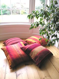 a pile of pillows sitting on top of a wooden floor next to a tree in front of a window