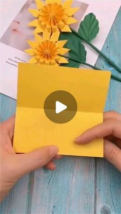 someone is holding up a yellow envelope with flowers in the background and video playing below