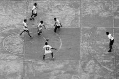 black and white photograph of men playing basketball on cement court with circle in center area