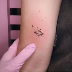 a small saturn tattoo on the left inner arm, with stars and planets around it