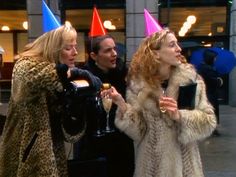 three women in party hats talking to each other on the sidewalk while holding wine glasses