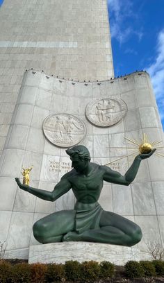 the statue is holding two golden balls in front of a tall building with three medallions on it