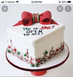 a white cake decorated with red bows and the words he or she open to see