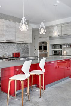 two white chairs sitting in front of a red kitchen island with lights hanging from the ceiling