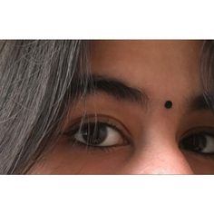 a close up of a woman's face with grey hair and black dots on her forehead