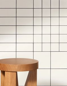 a wooden stool sitting in front of a white tiled wall