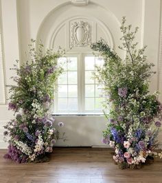 two tall flower arrangements sitting on top of a wooden floor in front of a window