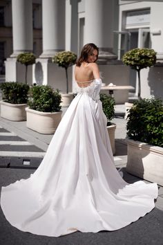 a woman in a white wedding dress standing on the street with her back to the camera