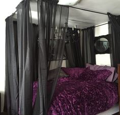 a bed with purple sheets and black drapes on the headboard, in a bedroom