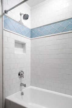 a white bath tub sitting next to a shower with blue tile on the walls and floor