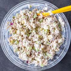 a glass bowl filled with tuna salad next to a yellow plastic spoon on a black surface