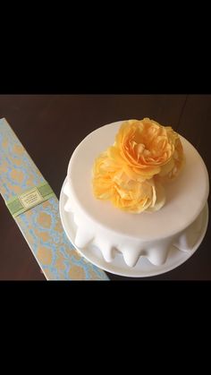 a white cake with yellow flowers on top sitting next to a blue and gold box