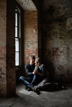 a man and woman are sitting on the floor in an old building with brick walls