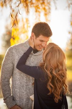 a man and woman standing next to each other in front of a tree with leaves