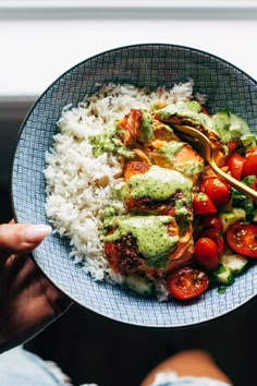 a person holding a plate with rice, tomatoes and chicken on it in front of a window