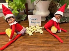 two elfs sitting on a table with popcorn and a sign that says fresh popcorn