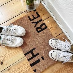 two pairs of white tennis shoes are sitting on a door mat that says, bye