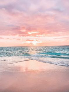 the sun is setting over the ocean with waves coming in to shore and pink clouds