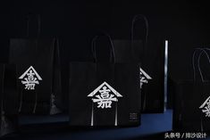 black shopping bags with white writing on them are lined up against a dark background, in the shape of a house