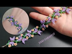 a hand is holding a beaded bracelet with purple flowers on it and green stems