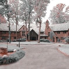 a large red brick house with lots of trees around the front yard and driveway area