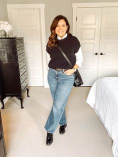 a woman standing in a bedroom next to a bed and dresser with a purse on her hip