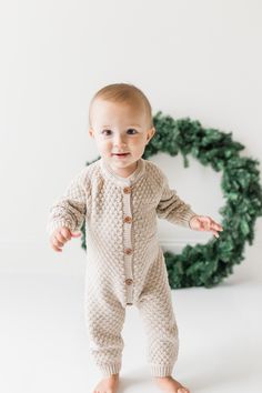 a baby standing in front of a christmas wreath