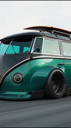 a green and black vw bus with surfboards on top is driving down the road