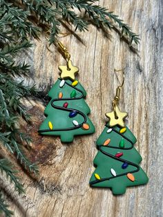 christmas tree earrings with lights on them sitting on a piece of wood next to evergreen branches