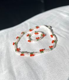 a beaded necklace with red and green beads is on a white cloth covered surface