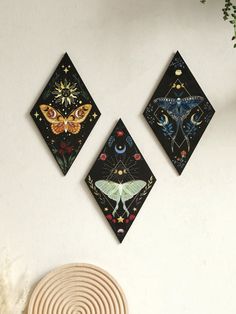 three square wall hangings with moths and stars on them, against a white wall