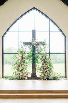 a cross with flowers on it in front of a large window at a wedding ceremony