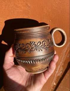 a hand holding a brown ceramic cup with ornate designs on the outside and inside, in front of a wooden door