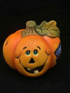 a ceramic pumpkin with green leaves on it's head and eyes, sitting in front of a black background