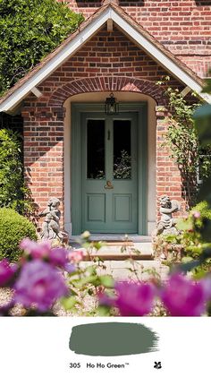 a green door in front of a red brick house with purple flowers around the doorway