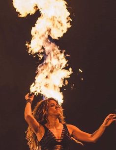 a woman with her arms up in the air and fire behind her, on stage